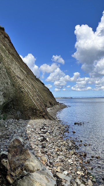Die Steilküste bei Ejerslev Havn mit einem schmalen Streifen Strand, den man entlang wandern kann. Blauer Himmel mit ein paar Wolken 